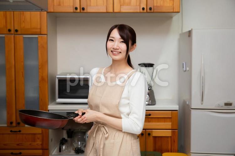 キッチンでフライパンを持っている笑顔の若い日本人女性 キッチン,台所,フライパンの写真素材