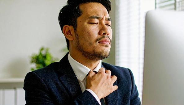 デスクワークで肩を回しほぐすビジネスマンの写真