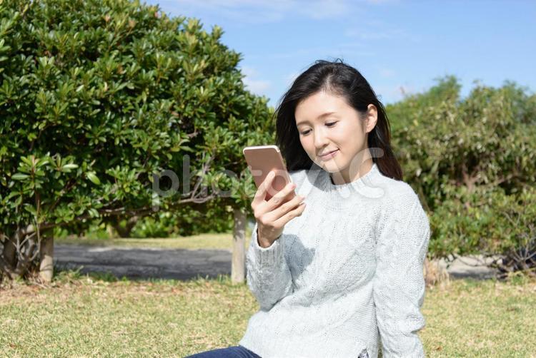 公園でスマートフォンを持って楽しむ女性 女性,スマホ,スマートフォンの写真素材