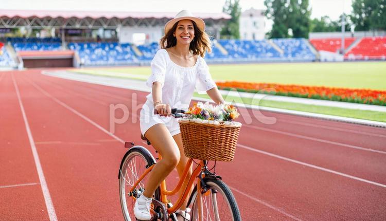 観客席の前を自転車に乗る帽子を被った女性 サイクル,サッカー場,サドルの写真素材