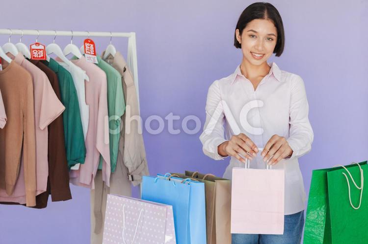 セールのタグの付いたハンガーに掛かった洋服と紙袋を持っている女性 セール,ショップ,女性の写真素材
