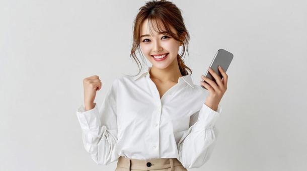 スマホを手に笑顔でガッツポーズする女性 スマホを手に笑顔でガッツポーズする女性の写真