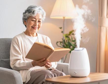 加湿器のそばで読書を楽しむシニア女性 加湿器のそばで読書を楽しむシニア女性の写真
