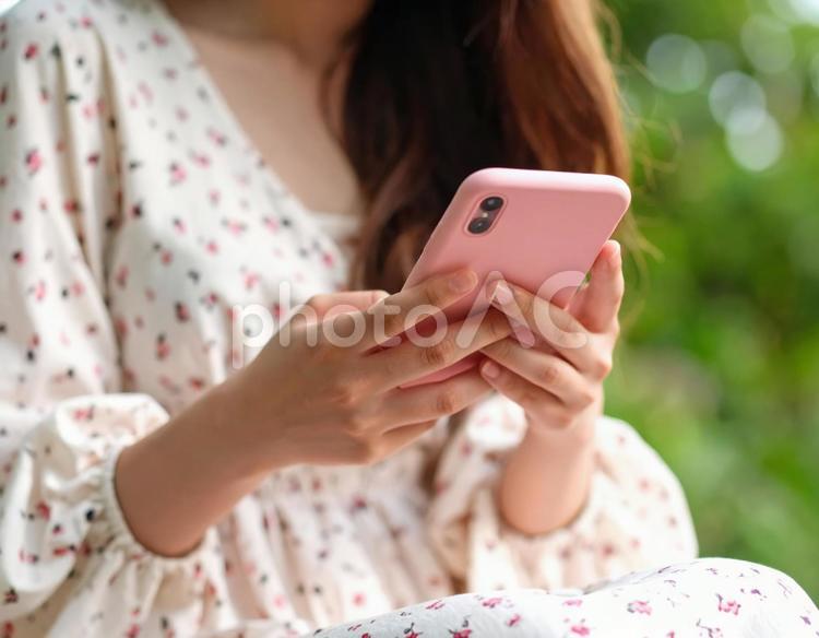座ってピンクのスマホを操作する女性の手元 スマホ,スマートフォン,女性の写真素材