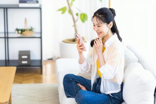 部屋でスマホを操作する女性 部屋でスマホを操作する女性 スマホ,笑顔,部屋の写真素材