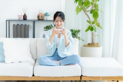 部屋でスマホを操作する若い女性 スマホ,笑顔,女性の写真素材