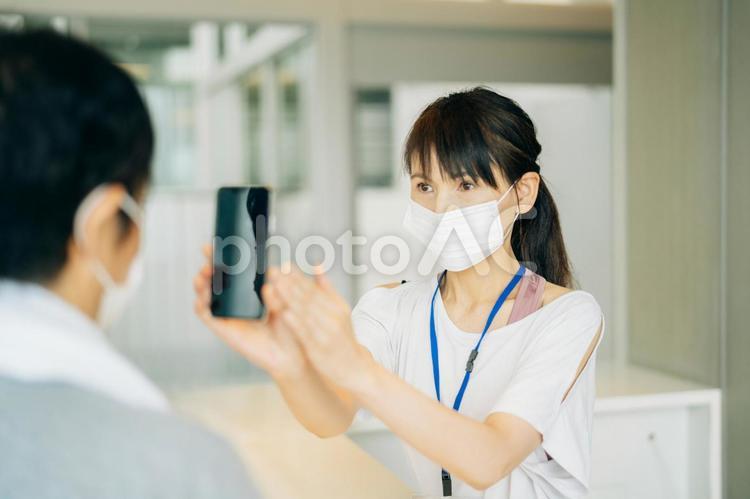 スポーツジムの受付をする女性（スマホ） 体温計,検温,スポーツジムの写真素材