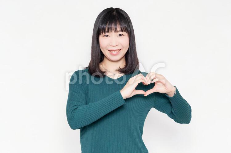 白背景の前に立って、手でハートの形を作る女性 女性,ハート,愛の写真素材