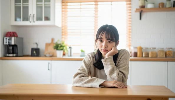 疲れた表情でキッチンに座る若い女性 疲れた表情でキッチンに座る若い女性の写真