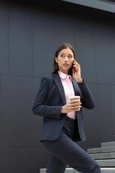 オフィスビルの外の階段でコーヒー片手に電話するビジネスウーマン ビジネスウーマン,ビジネス,女性の写真素材