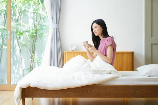 ベッドで真剣な顔でスマホを持つ横向き女性 女性,スマートフォン,持つの写真素材