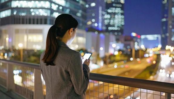 会社帰りにスマホを見るビジネスウーマン 会社帰りにスマホを見るビジネスウーマンの写真