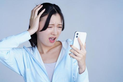 水色の服の女性がスマホを見て頭を抱える 女性,スマートフォン,持つの写真素材