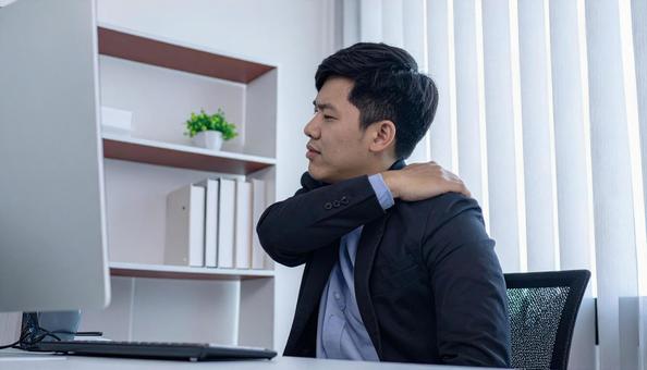 デスクワークで肩を回しほぐすビジネスマンの写真