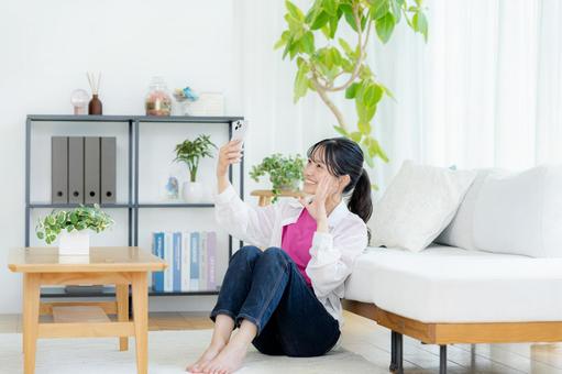 部屋でスマホを操作する若い女性 スマホ,笑顔,若い女性の写真素材
