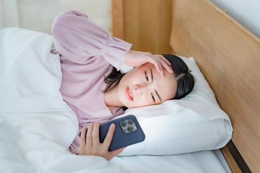 ベッドで携帯を見て困る女性 ベッドで携帯を見て困る女性 携帯電話,トラブル,夜更しの写真素材