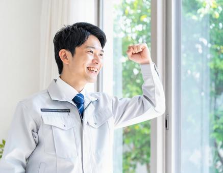窓辺でガッツポーズをする若い作業服の男性の写真