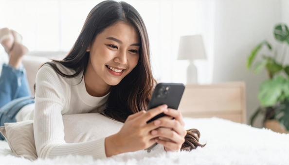リビングで横になりスマホを操作する女性 リビングで横になりスマホを操作する女性の写真