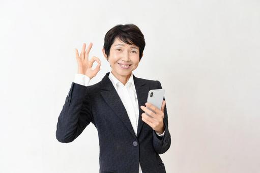 スマホを持ちOKするスーツ姿のミドル女性 中高年,スマホ,ビジネスの写真素材