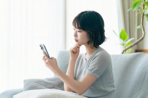 スマホを見て考えごとをする女性 女性,スマホ,スマートフォンの写真素材