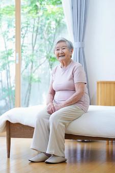 窓際のベッドの布団に座り笑う高齢女性 女性,ベッド,座るの写真素材