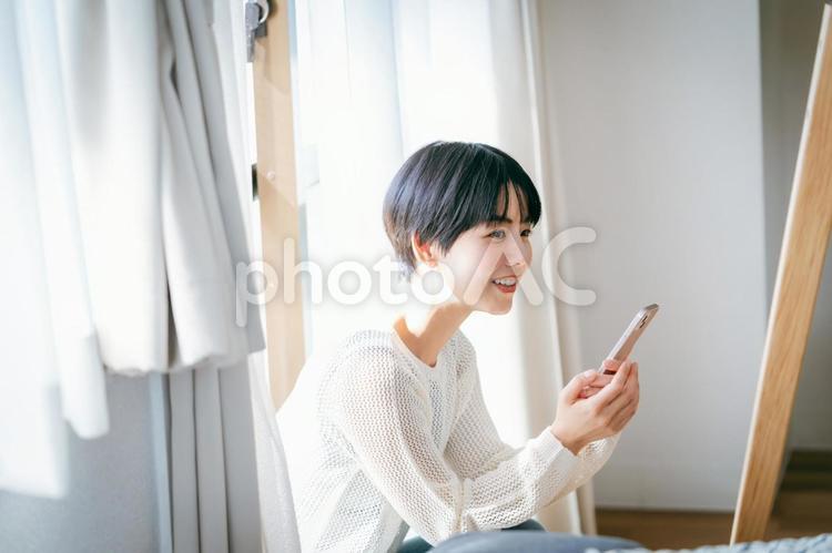部屋でスマホを操作する女性 スマホ,笑顔,女性の写真素材