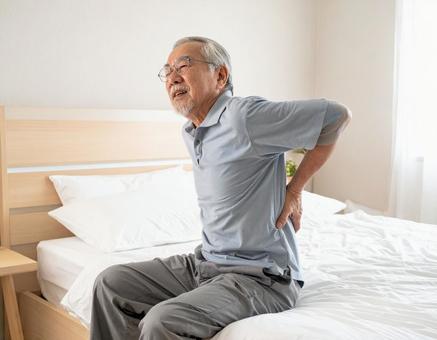 ベットの上で腰を抑えて苦しむシニア男性 ベットの上で腰を抑えて苦しむシニア男性の写真