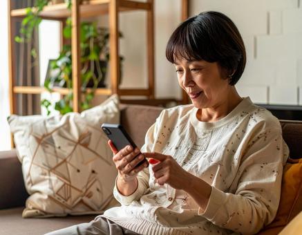 自宅でスマホを操作するシニア女性の写真