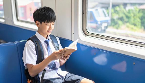 電車内で読書する男子学生の写真