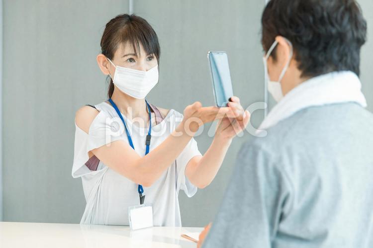 スポーツジムの受付をする女性（スマホ） 体温計,検温,スポーツジムの写真素材