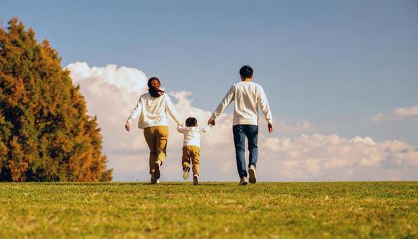 秋の公園を歩く家族の後ろ姿の写真