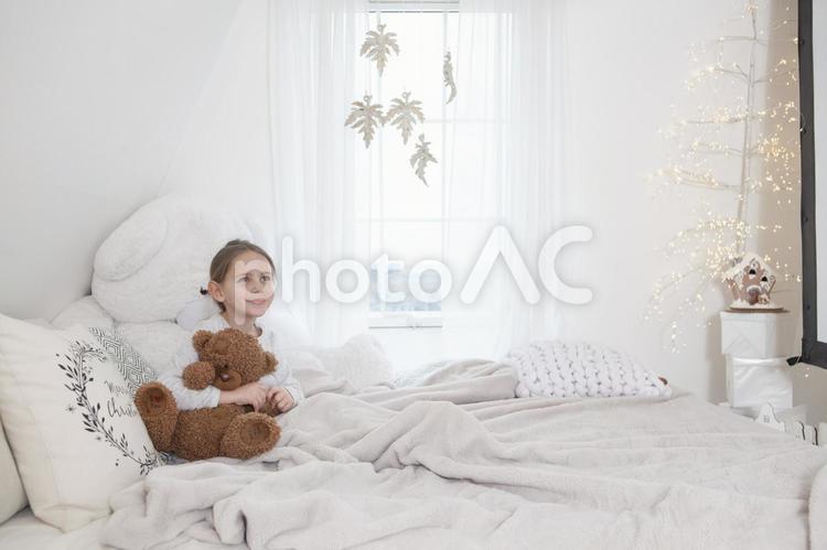 クマのぬいぐるみを抱っこしてベッドに座っている女の子 子ども,女の子,外国人の写真素材