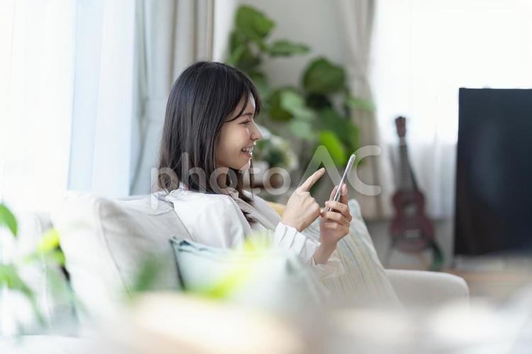 ソファで携帯を持つ日本人女性 スマホ,スマートフォン,操作の写真素材
