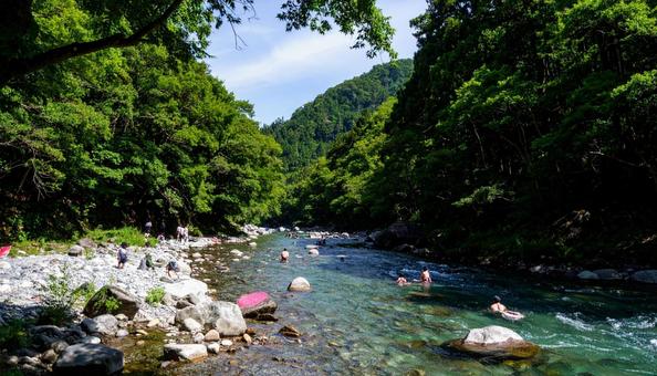 夏の渓谷の水辺で涼をとる人たちの写真