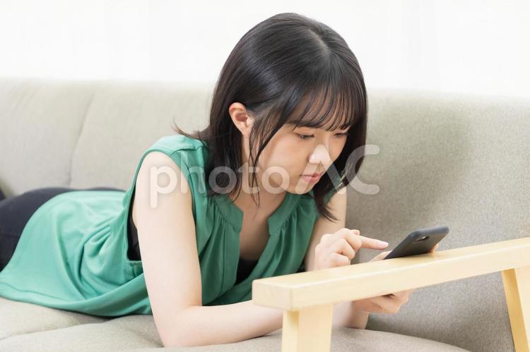 ソファに寝転んでスマホを使う若い女性 スマホ,若い,女性の写真素材