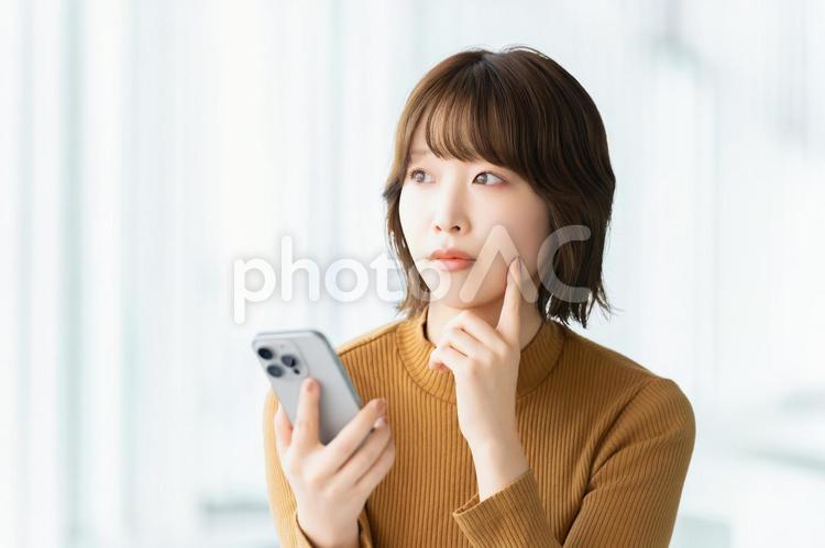 スマホを持って考える女性 女性,困る,考えるの写真素材