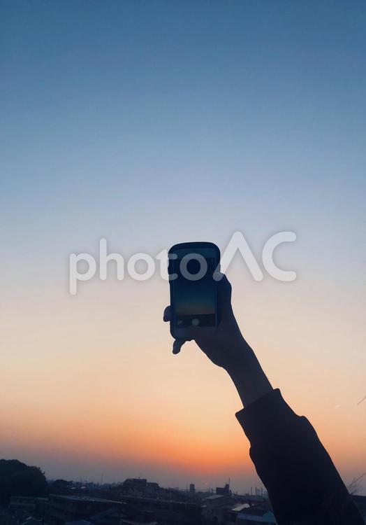 夕焼けの空をスマホで撮影する人 日暮れ,旅,空の写真素材