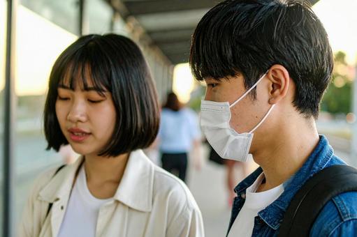 バス停で会話しながらバスを待つ男女 バス停で会話しながらバスを待つ男女の写真