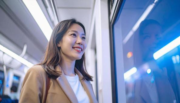 夜、電車内から外を見る日本人女性の写真
