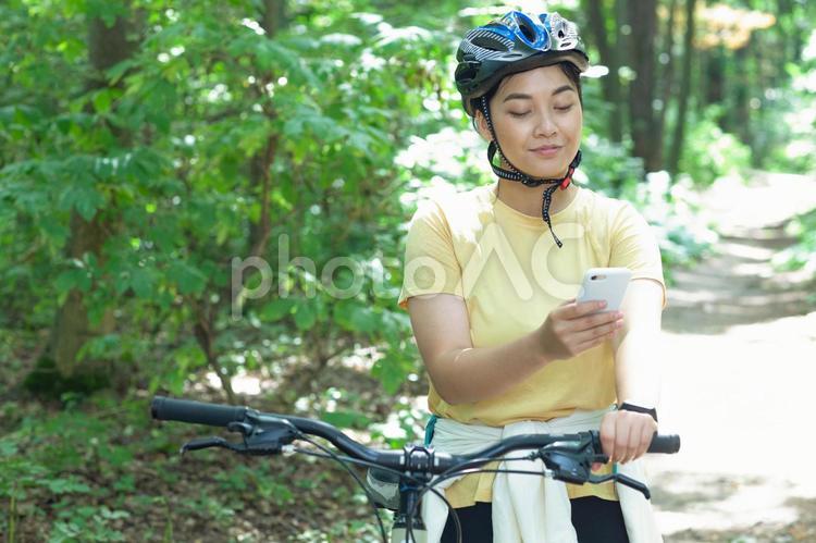自転車から降りてスマホを使う女性 自転車,サイクリング,女性の写真素材