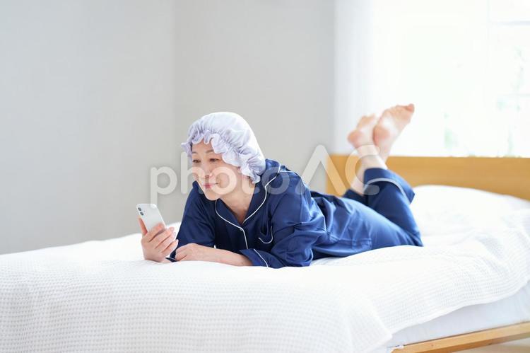 ベッドでスマートフォンを見ながらくつろぐ中年女性 主婦,人物,女性の写真素材