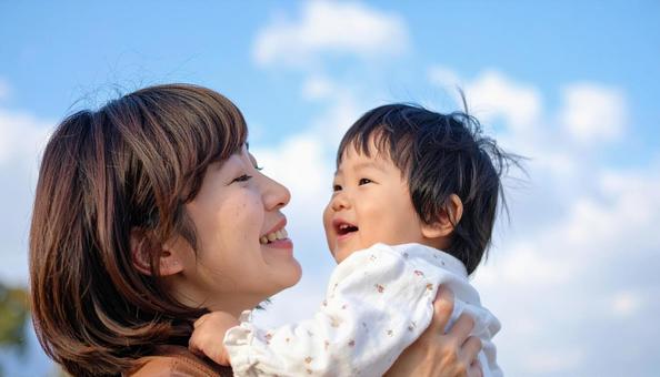 青空の下、子供を抱っこする母親 青空の下、子供を抱っこする母親の写真
