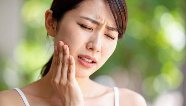 歯が痛んで手で押さえる女性の写真