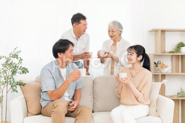 ソファに座って飲み物を飲む家族（話す） 家族,親子,お茶の写真素材