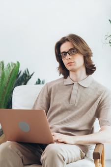 椅子に座って膝の上でノートパソコンをっているカメラ目線の若い男性 男性,外国人,欧米人の写真素材