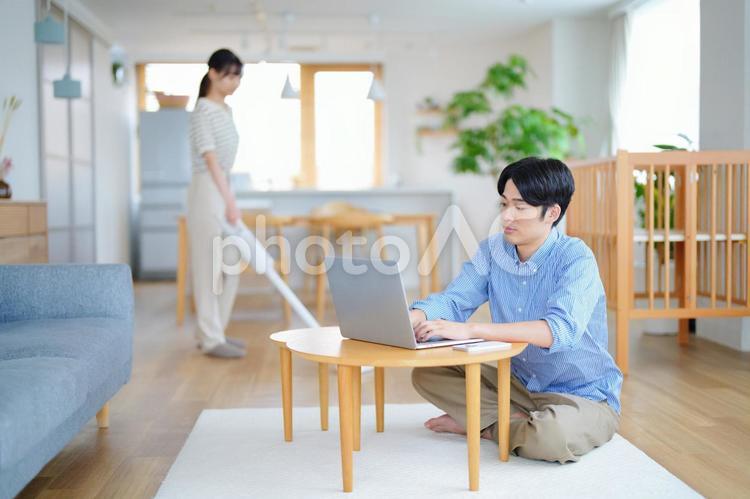 胡坐でパソコンをする男性と掃除中の女性 男性,ノートパソコン,テレワークの写真素材