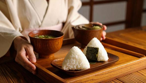 お盆に乗ったおにぎりと味噌汁を持つ女性の写真