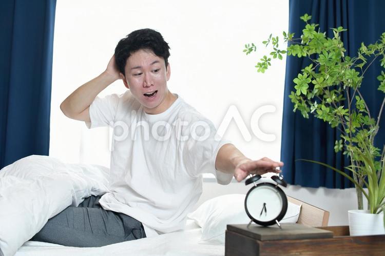 慌ててベッドから起きるアジア人の若い男性 寝坊,朝寝坊,起床の写真素材