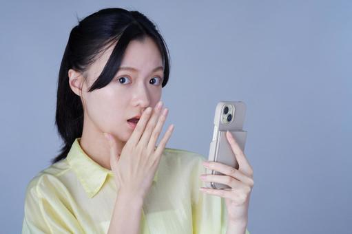 スマホをもって口元を隠す黄色い服の女性 女性,スマートフォン,持つの写真素材
