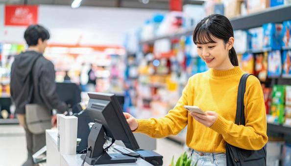 スーパーでスマホ決済を使う若い日本人女性 スーパーでスマホ決済を使う若い日本人女性の写真